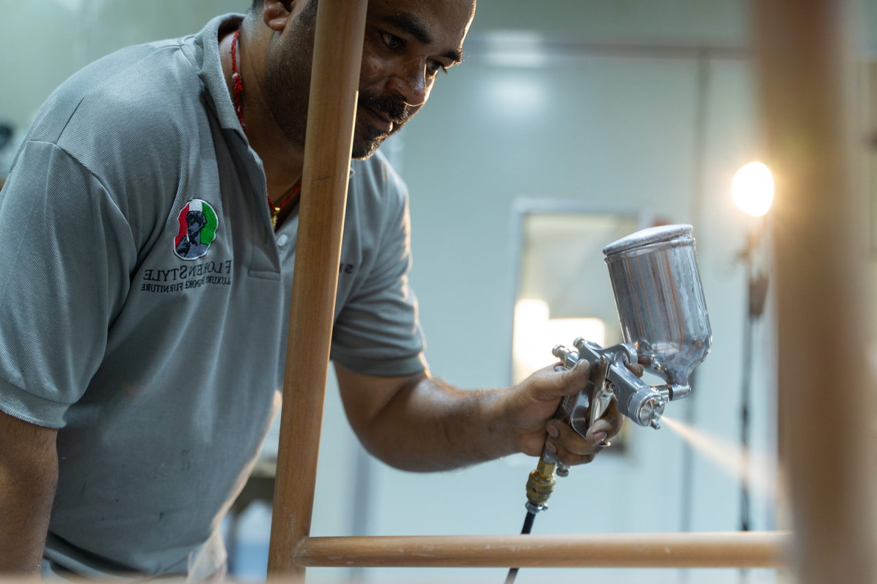 A FlorenStyle craftsman hand-spraying a lacquer finish onto a timber frame in the finishing bay