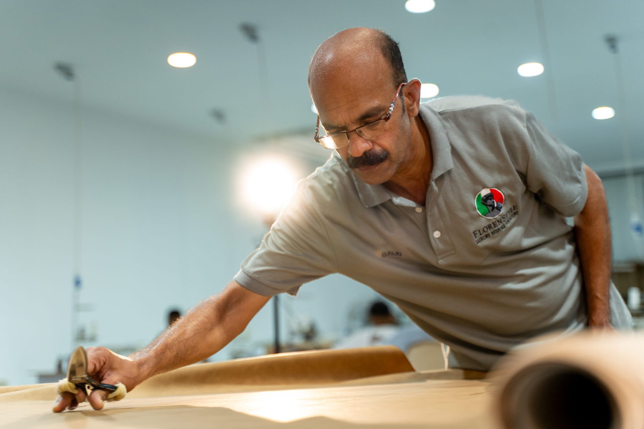 A master upholsterer marking and cutting a full leather hide by hand on the cutting table