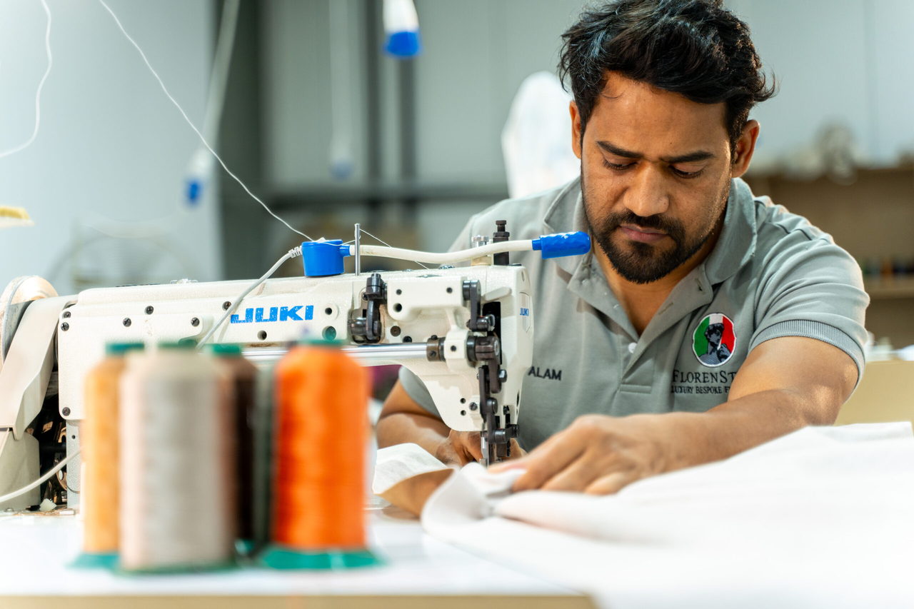 An upholsterer guiding fabric through an industrial sewing machine, with cones of thread in the foreground