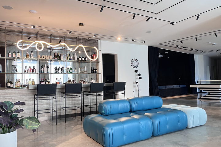 A hotel bar with a sculptural neon-lit back bar, blue modular seating and bespoke bar stools