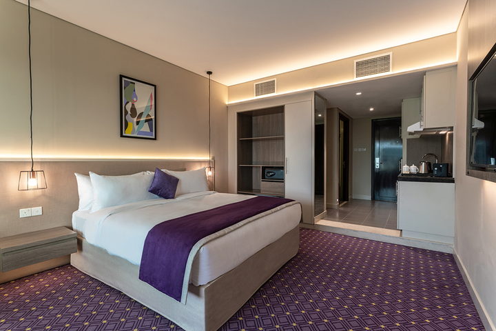 A hotel suite with a bespoke upholstered headboard, fitted joinery and a tailored bed runner