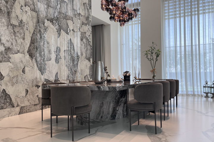 A dining room set against a book-matched marble wall, with a dark timber table and upholstered chairs