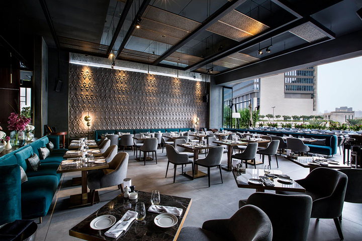 A restaurant dining room with teal velvet banquettes, bronze mesh screens and bespoke dining chairs